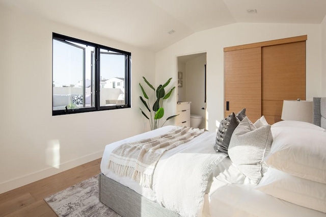 bedroom featuring vaulted ceiling, a closet, ensuite bathroom, and light hardwood / wood-style flooring