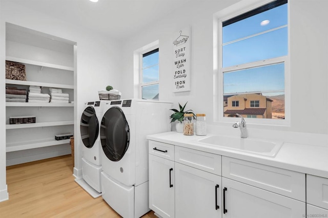 laundry room with washer and clothes dryer, a healthy amount of sunlight, cabinets, light hardwood / wood-style flooring, and sink