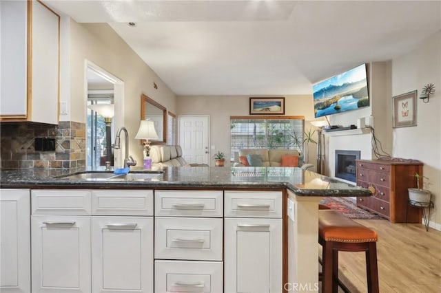 kitchen featuring white cabinets, kitchen peninsula, sink, and dark stone countertops