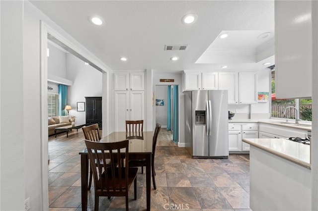 kitchen with a raised ceiling, sink, crown molding, white cabinetry, and stainless steel fridge with ice dispenser