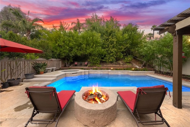 pool at dusk with an outdoor fire pit, a patio area, and an in ground hot tub