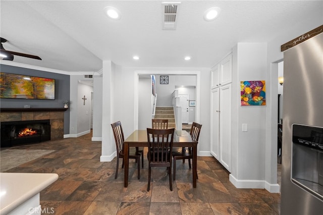 dining room featuring ceiling fan, a tiled fireplace, crown molding, and a textured ceiling