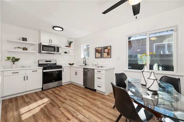 kitchen featuring appliances with stainless steel finishes, white cabinetry, sink, ceiling fan, and light hardwood / wood-style flooring