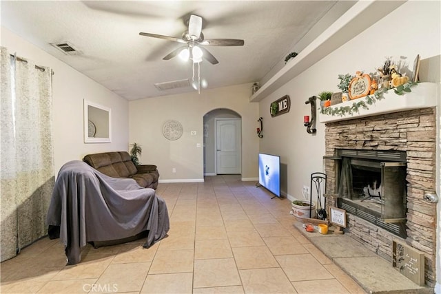 tiled living room featuring a stone fireplace, a textured ceiling, and ceiling fan