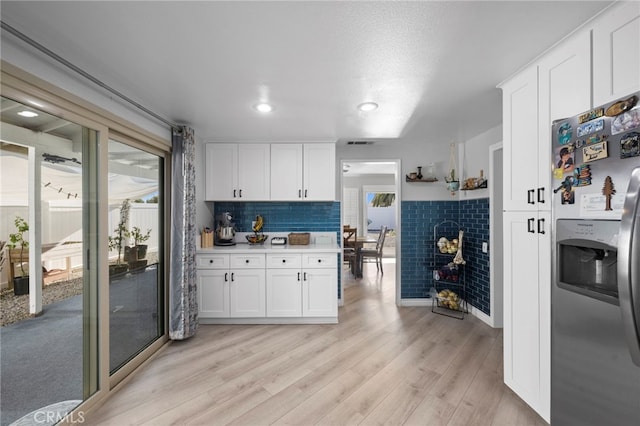 kitchen featuring a tile fireplace, white cabinetry, stainless steel refrigerator with ice dispenser, light hardwood / wood-style floors, and decorative backsplash