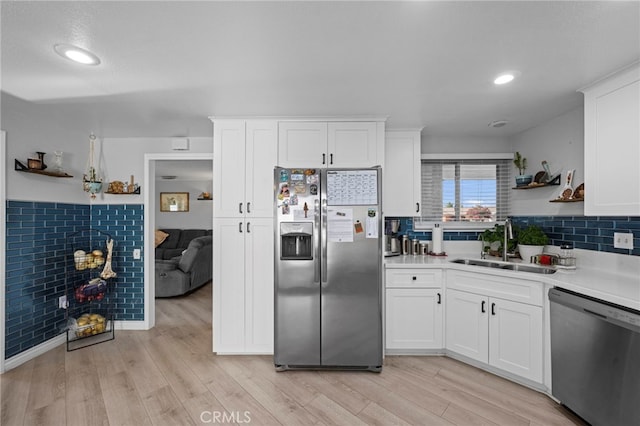 kitchen with sink, backsplash, white cabinets, stainless steel appliances, and light wood-type flooring