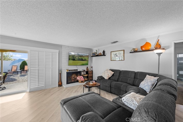 living room with ornamental molding, a brick fireplace, a textured ceiling, and light hardwood / wood-style floors