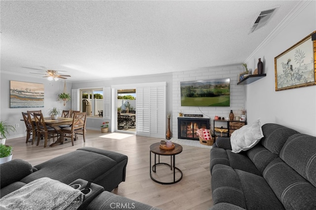 living room featuring a fireplace, ceiling fan, crown molding, a textured ceiling, and light wood-type flooring