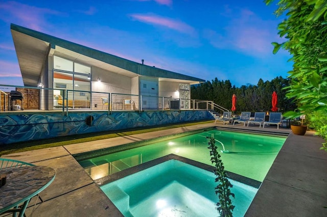 pool at dusk featuring an in ground hot tub and a patio area