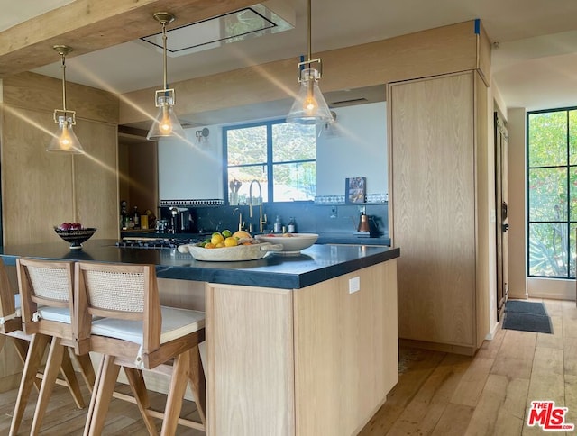 kitchen with light wood-type flooring, backsplash, light brown cabinets, and hanging light fixtures