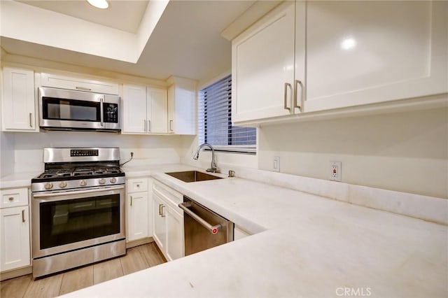 kitchen with appliances with stainless steel finishes, white cabinetry, sink, a raised ceiling, and light hardwood / wood-style flooring