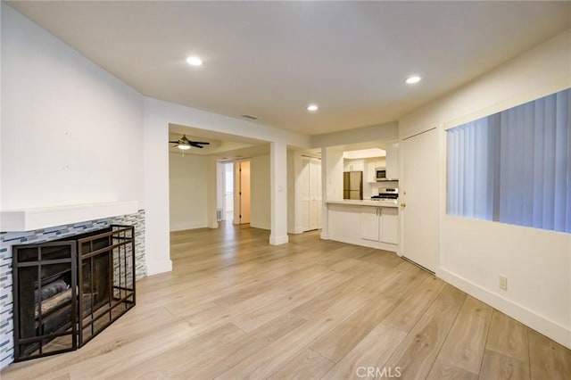 living room featuring ceiling fan, light hardwood / wood-style floors, and a stone fireplace