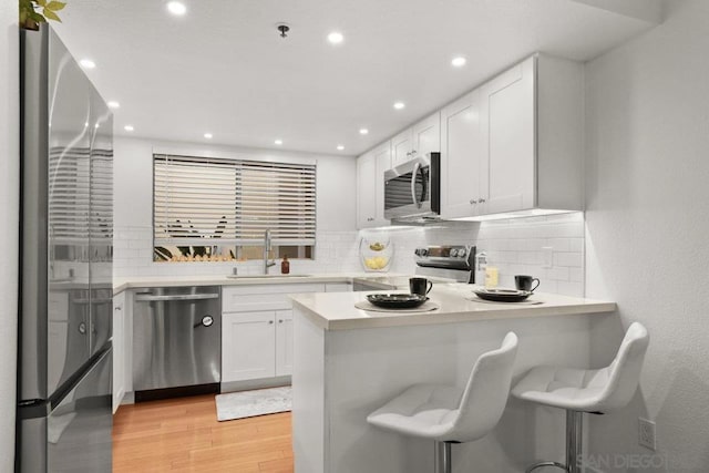 kitchen with kitchen peninsula, sink, appliances with stainless steel finishes, a kitchen breakfast bar, and white cabinets