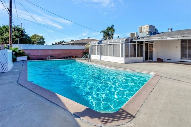 view of swimming pool with cooling unit, a sunroom, and a patio