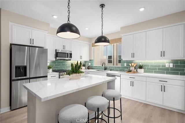 kitchen with pendant lighting, a kitchen island, sink, white cabinetry, and appliances with stainless steel finishes