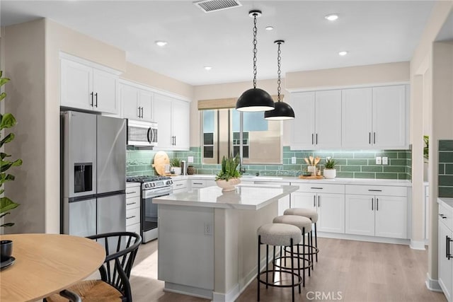 kitchen with decorative light fixtures, a center island, white cabinetry, light hardwood / wood-style flooring, and stainless steel appliances