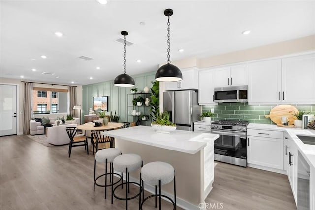 kitchen featuring appliances with stainless steel finishes, a center island, white cabinetry, and decorative light fixtures