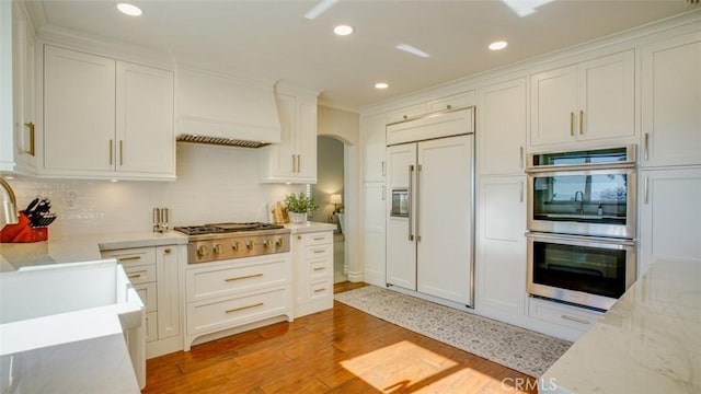 kitchen featuring white cabinetry, appliances with stainless steel finishes, tasteful backsplash, light wood-type flooring, and custom range hood