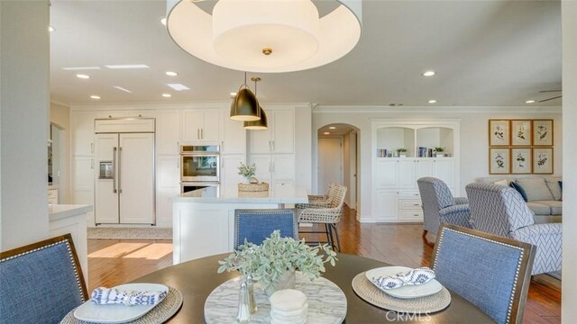 dining area with built in shelves, ornamental molding, and light hardwood / wood-style flooring