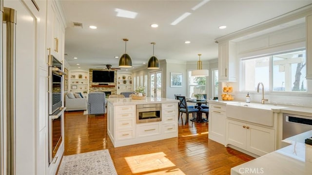 kitchen featuring stainless steel appliances, built in features, hanging light fixtures, white cabinets, and sink