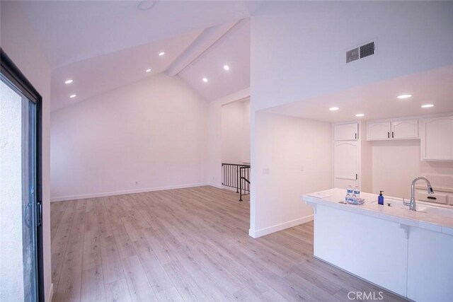 interior space with vaulted ceiling with beams, sink, light hardwood / wood-style flooring, and white cabinets