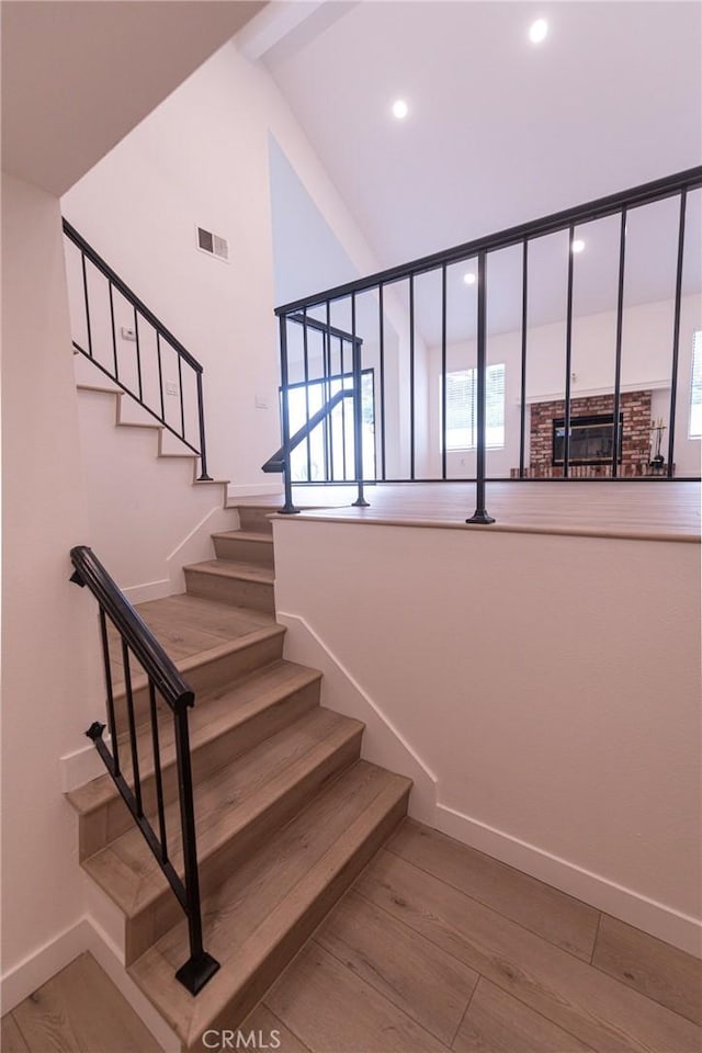 stairs with hardwood / wood-style floors and high vaulted ceiling