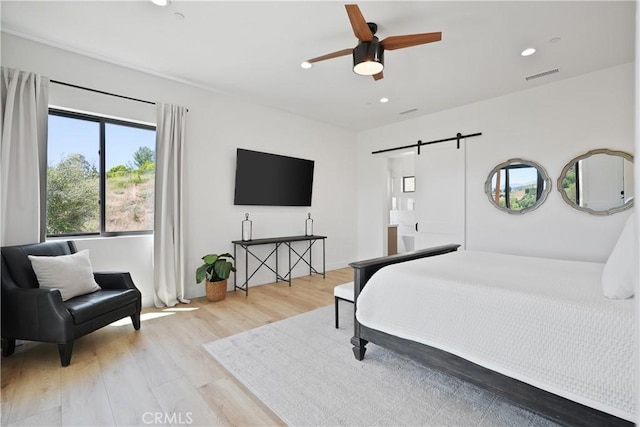 bedroom with ceiling fan, a barn door, and light wood-type flooring