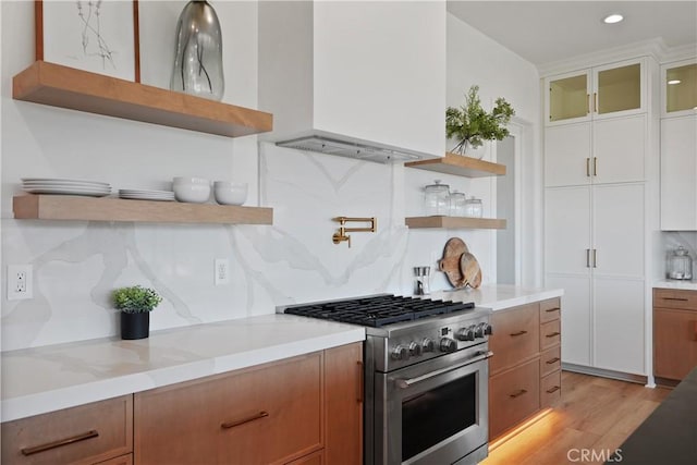 kitchen featuring high end stainless steel range, tasteful backsplash, light wood-type flooring, light stone countertops, and white cabinets