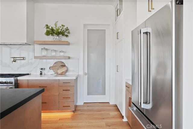 kitchen with decorative backsplash, high quality appliances, and light hardwood / wood-style flooring