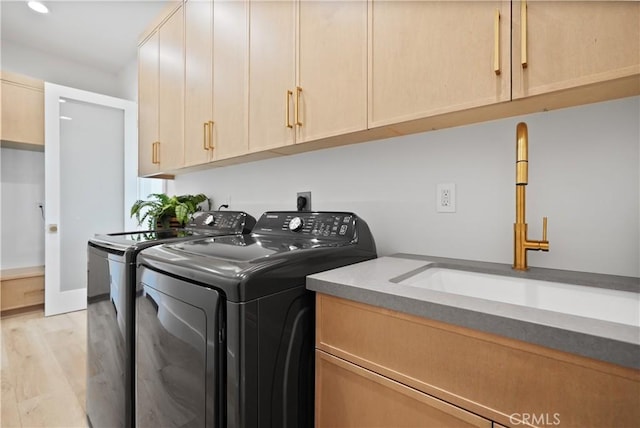 laundry area with sink, washer and dryer, light hardwood / wood-style floors, and cabinets