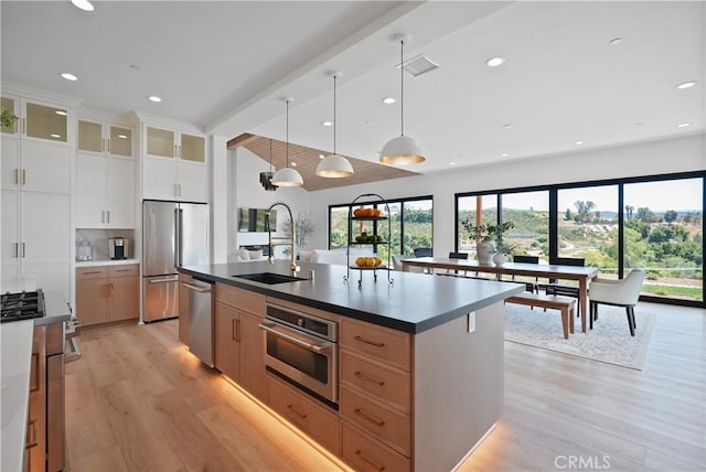 kitchen with pendant lighting, a center island with sink, sink, stainless steel appliances, and white cabinets