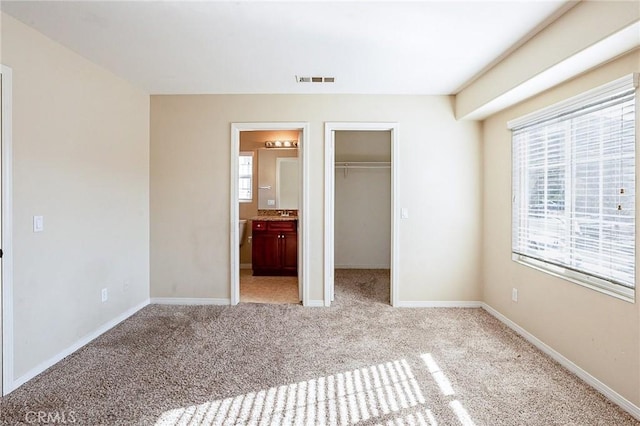 unfurnished bedroom with a spacious closet, light colored carpet, a closet, and connected bathroom