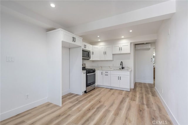 kitchen featuring a wall mounted AC, light hardwood / wood-style floors, sink, appliances with stainless steel finishes, and white cabinets