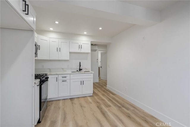 kitchen with gas range, light hardwood / wood-style floors, white cabinetry, and sink