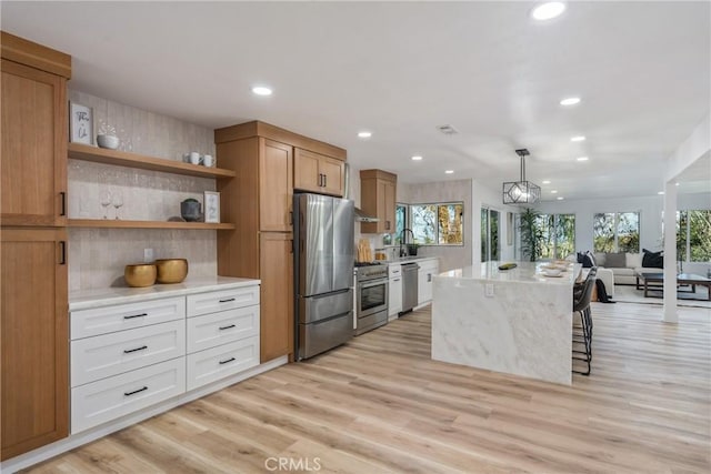 kitchen featuring sink, white cabinetry, hanging light fixtures, light wood-type flooring, and appliances with stainless steel finishes