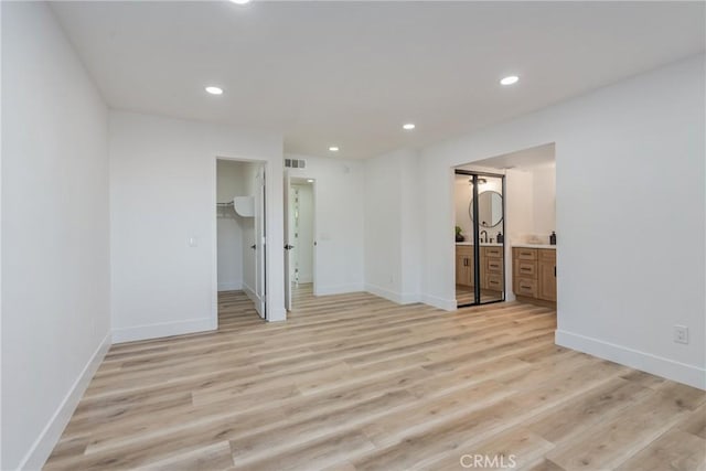 unfurnished bedroom featuring a closet, a walk in closet, light hardwood / wood-style flooring, and ensuite bath