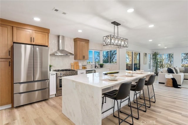 kitchen with a kitchen bar, stainless steel appliances, wall chimney range hood, a kitchen island, and light hardwood / wood-style flooring