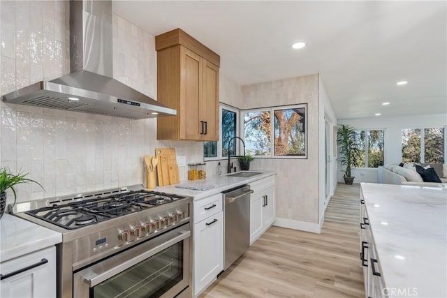 kitchen with wall chimney range hood, light hardwood / wood-style floors, sink, appliances with stainless steel finishes, and white cabinets