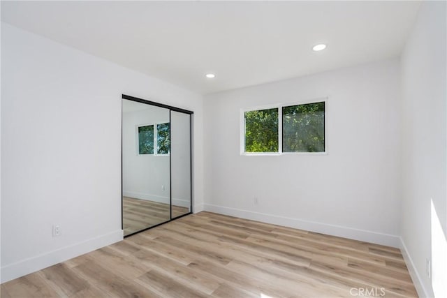 unfurnished bedroom with light wood-type flooring, a closet, and multiple windows