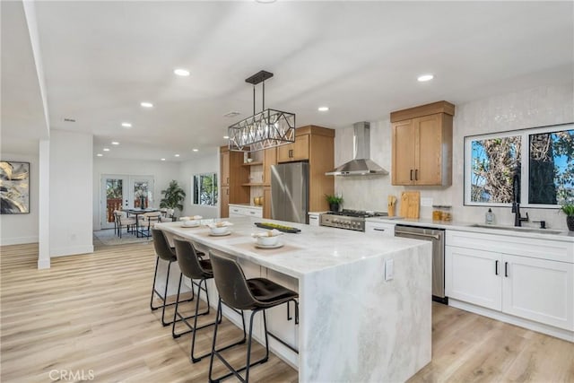 kitchen with pendant lighting, appliances with stainless steel finishes, wall chimney exhaust hood, a kitchen island, and white cabinetry