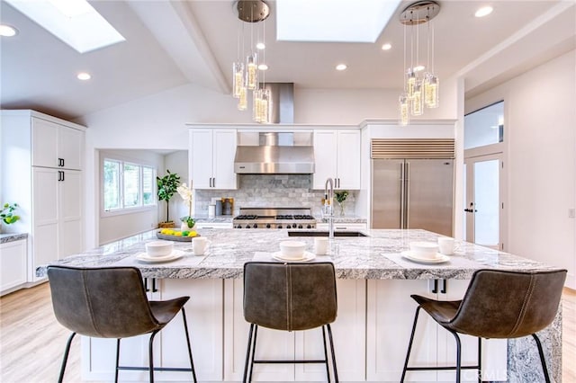 kitchen featuring a spacious island, pendant lighting, white cabinetry, stainless steel built in fridge, and wall chimney exhaust hood