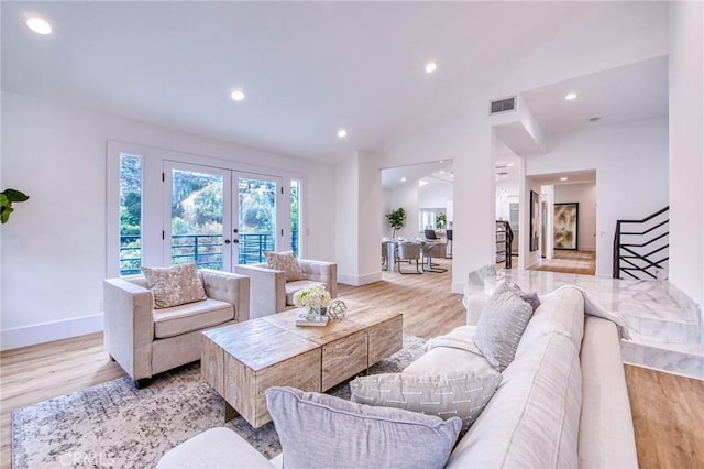 living room with vaulted ceiling, light hardwood / wood-style floors, and french doors