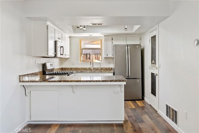 kitchen with kitchen peninsula, stainless steel appliances, dark stone countertops, and white cabinetry