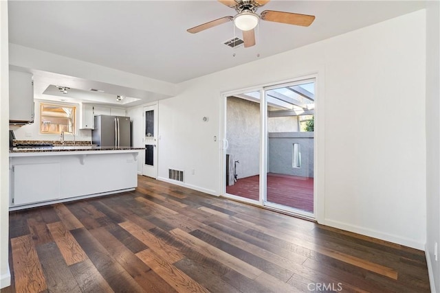 kitchen featuring dark wood-type flooring, kitchen peninsula, white cabinetry, and stainless steel fridge