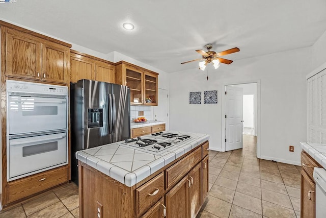 kitchen featuring tile counters, a kitchen island, stainless steel refrigerator with ice dispenser, double oven, and gas cooktop