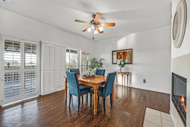 dining room featuring ceiling fan, wood-type flooring, and a tile fireplace