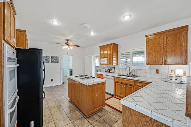 kitchen with tile countertops, a kitchen island, decorative backsplash, sink, and white appliances