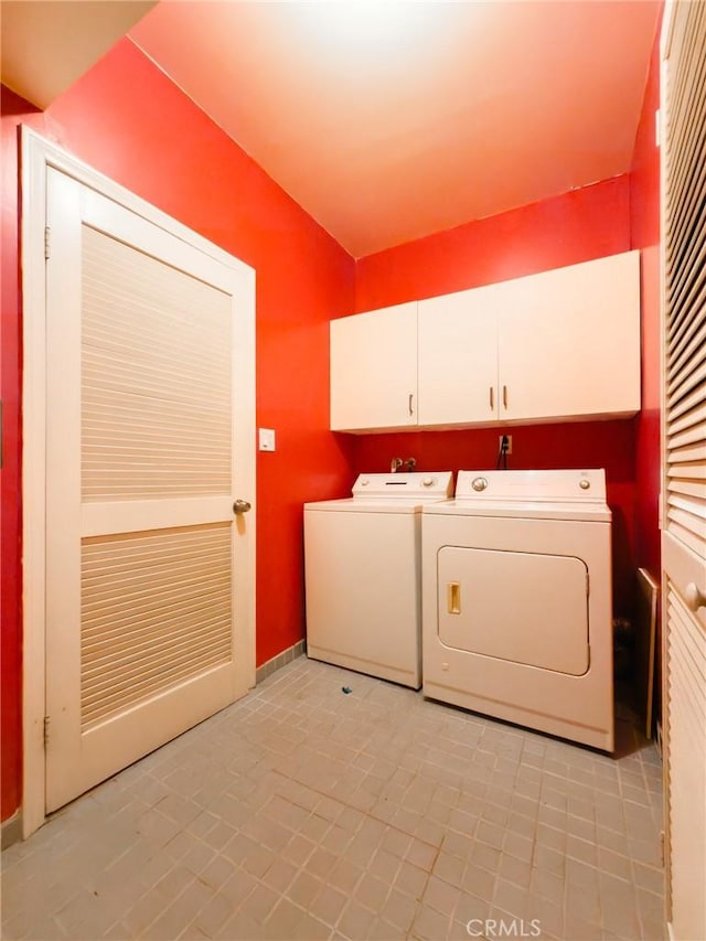 clothes washing area with cabinets, light tile patterned floors, and washing machine and dryer