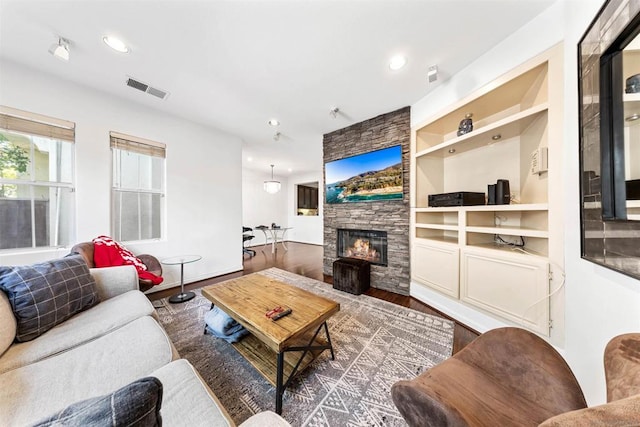 living room featuring built in shelves, dark hardwood / wood-style flooring, and a stone fireplace