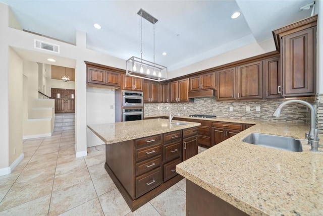 kitchen featuring decorative light fixtures, a kitchen island, sink, light stone countertops, and double oven